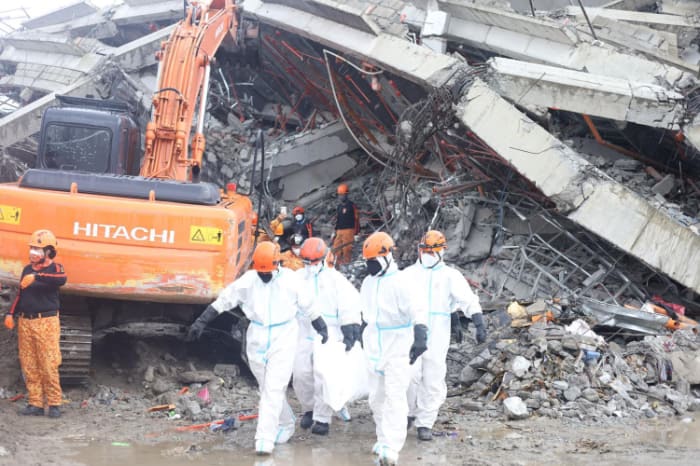 １日午後１時ごろにビル倒壊現場から13人目となる犠牲者の遺体を運び出す捜索隊員ら